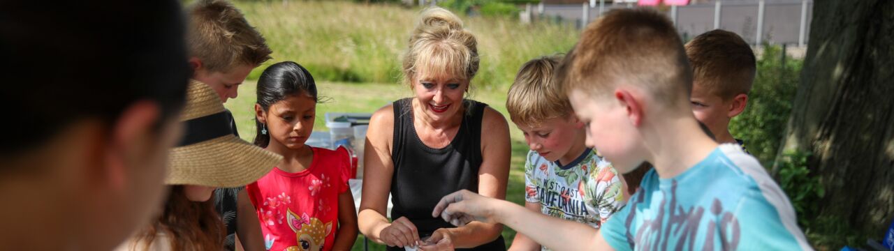 Keramiekdocente zit te midden van een groep kinderen met knutselmaterialen op tafel.