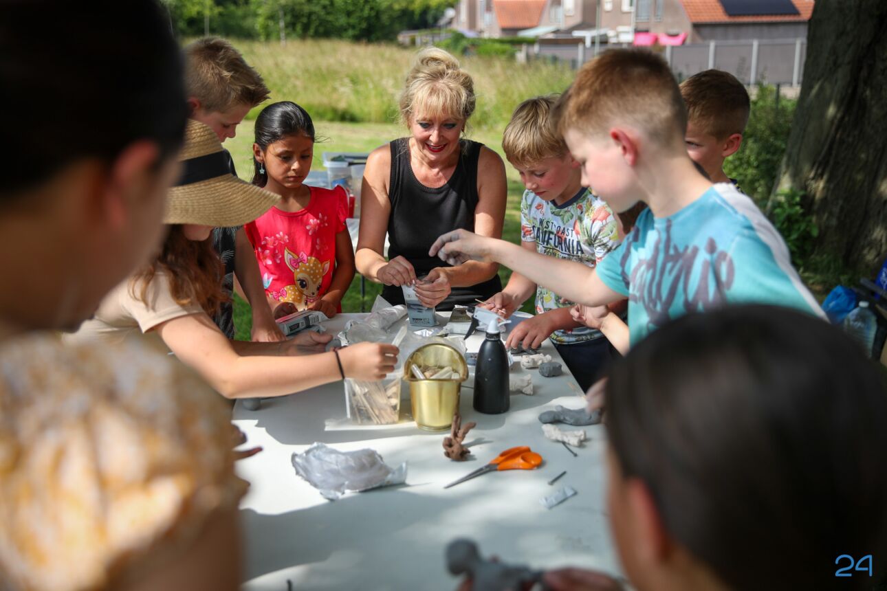 Keramiekdocente zit te midden van een groep kinderen met knutselmaterialen op tafel.