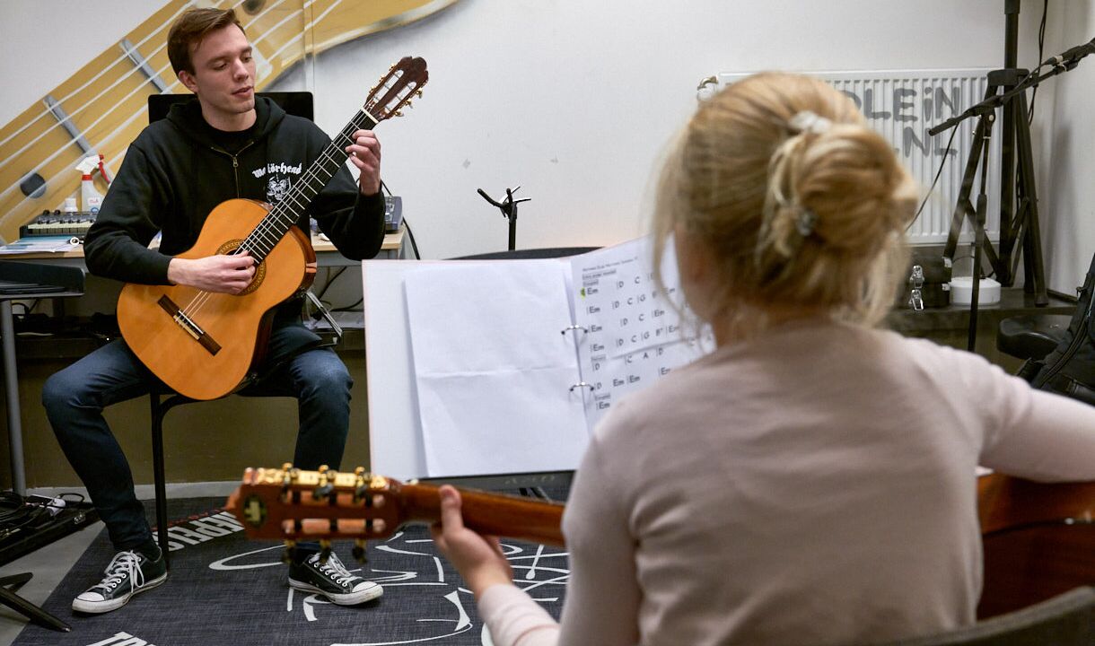 Leerling krijgt gitaarles van docent
