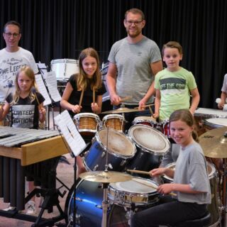 Een slagwerkgroep met kinderen en twee volwassen begeleiders poseren voor de foto.