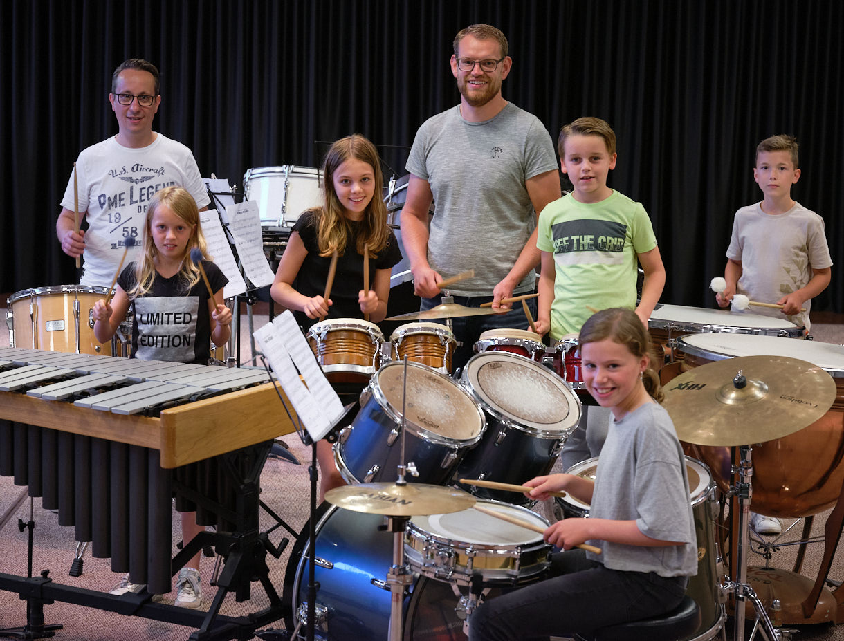 Een slagwerkgroep met kinderen en twee volwassen begeleiders poseren voor de foto.