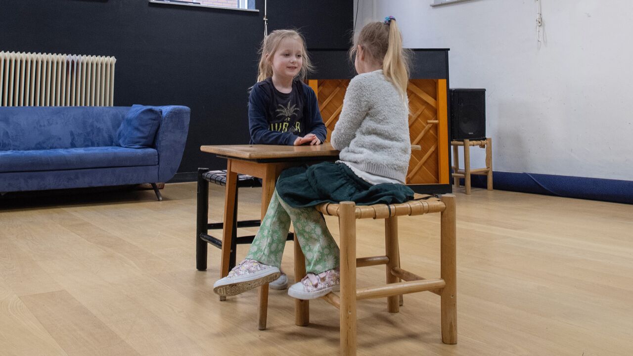 Twee kindjes zitten in een toneelles aan een tafel