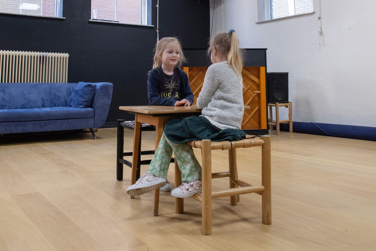 Twee kindjes zitten in een toneelles aan een tafel